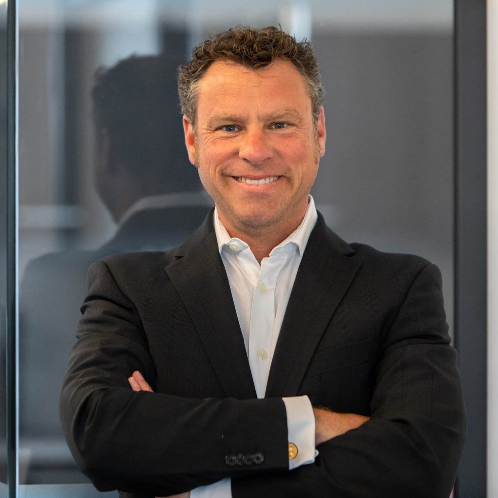 Michael Liebermann, Geschäftsführer der tegos Holding GmbH, im Anzug mit verschränkten Armen vor Glaswand.