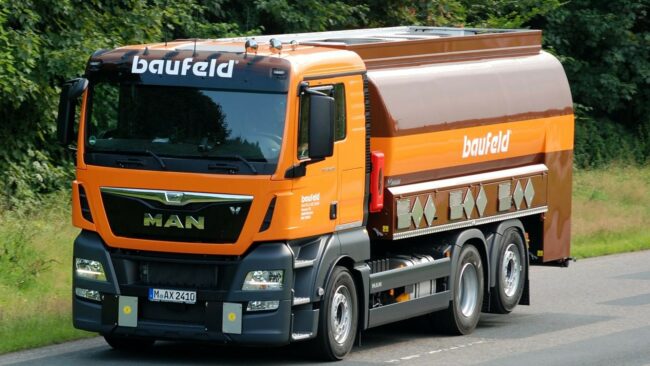 baufeld Tankfahrzeug der baufeld GmbH in orange-brauner Lackierung auf Landstraße.