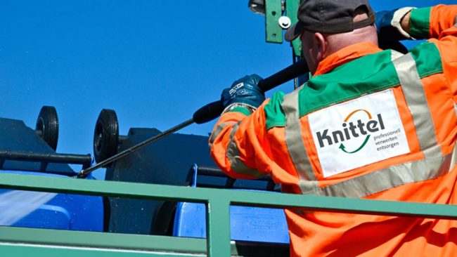 knittel-entsorgung-enwis3 Ein Mitarbeiter der Firma Knittel reinigt mit einem Hochdruckreiniger blaue Mülltonnen.