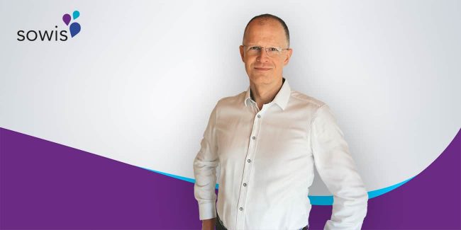 Ingo Hoffmann, Mitarbeiter bei sowis, steht vor einem Hintergrund mit sowis-Logos und lila-blauem Design und trägt ein weißes Hemd.