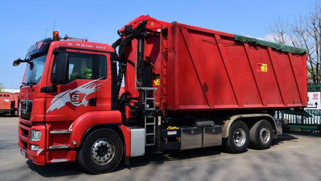 enwis-Update-bei-der-Stark-GmbH Roter LKW der STARK GmbH mit Containeraufbau auf dem Firmengelände. Das Unternehmen setzt auf ein aktuelles enwis-Update zur Optimierung seiner Entsorgungsprozesse.