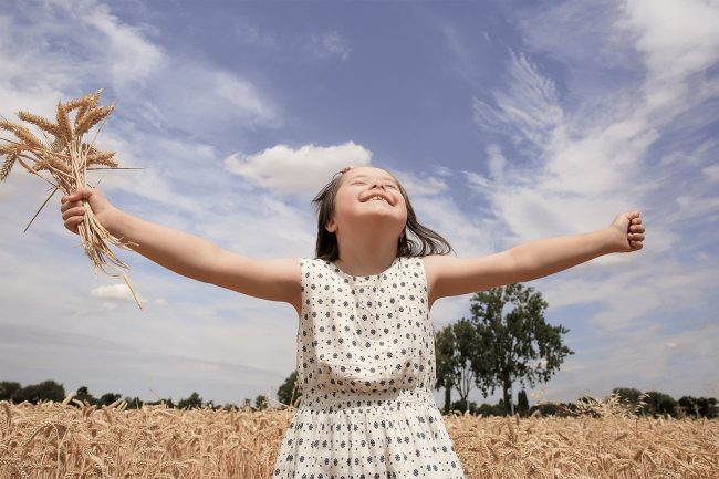 Blog-sowis_1300x866_sowisABRECHNUNG Lachendes Mädchen steht mit ausgebreiteten Armen in einem Weizenfeld und hält Getreidehalme in der Hand.