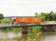 Orangener LKW der Städtereinigung Ernst fährt über eine Brücke in grüner Umgebung.