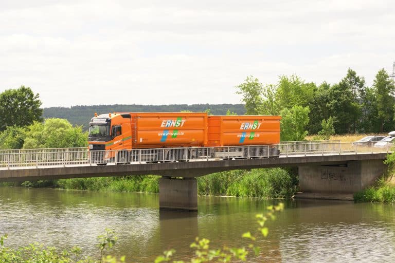 Orangener LKW der Städtereinigung Ernst fährt über eine Brücke in grüner Umgebung.