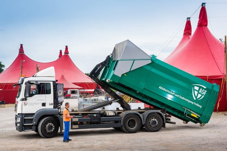 Containerfahrzeug der ASF Freiburg beim Absetzen eines Abrollbehälters vor einem roten Zirkuszelt.