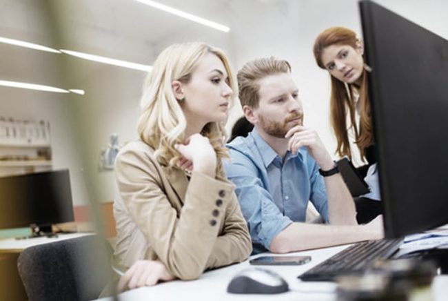 neue-funktionen-in-sowisabrechnung Drei Personen im Büro schauen gemeinsam konzentriert auf einen Computerbildschirm.