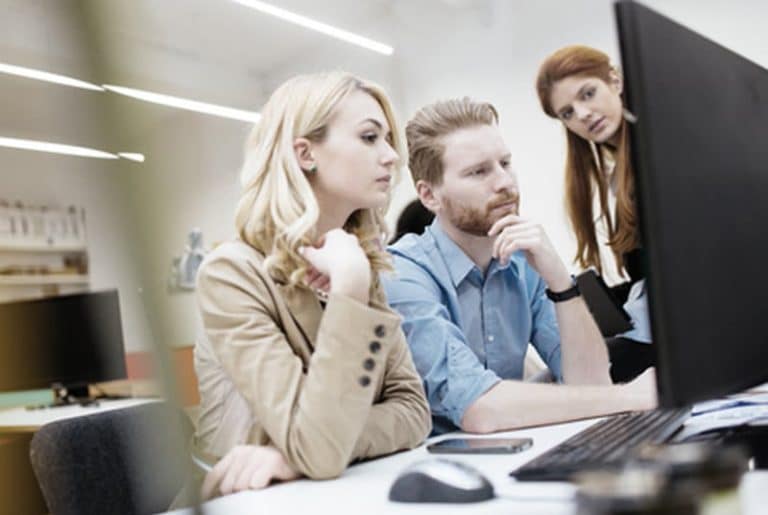 Drei Personen im Büro schauen gemeinsam konzentriert auf einen Computerbildschirm.