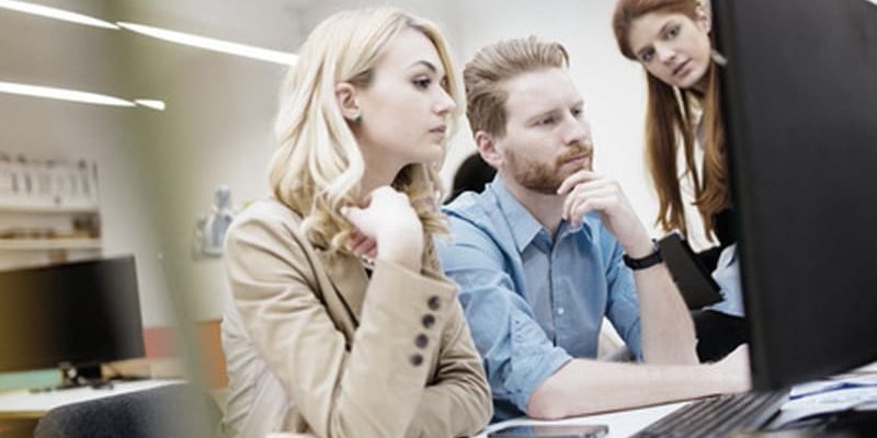 Drei Personen im Büro schauen gemeinsam konzentriert auf einen Computerbildschirm.
