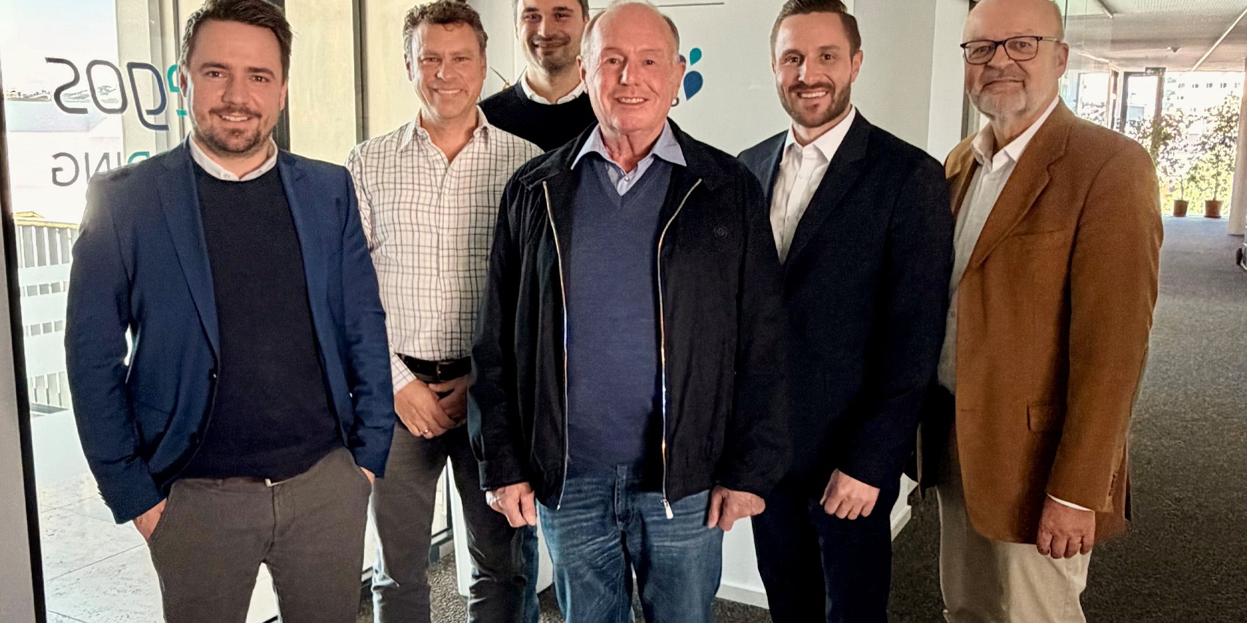 Siebte Beiratssitzung der tegos Holding. Daniel Artmann, Doktor Walter, Arthur Krautbauer, Professor Doktor B Niestroj, Maximilian Krautbauer und Michael Liebermann stehen vor einer Glaswand mit tegos Holding Logo nach einer erfolgreichen, gemeinsamen Sitzung.