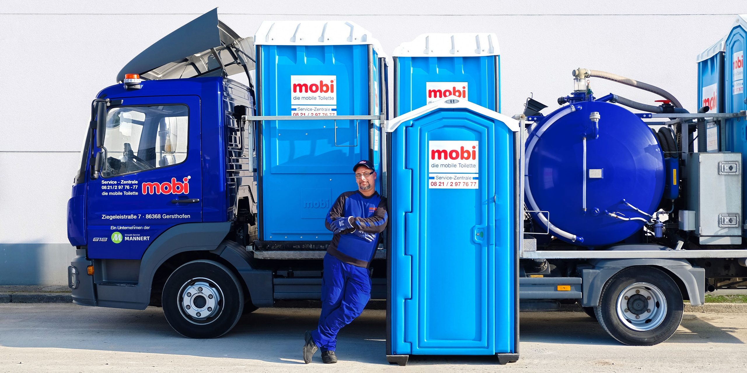 Ein Mann lehnt sich an eine mobile mobi Toilette vor einem Fahrzeug.