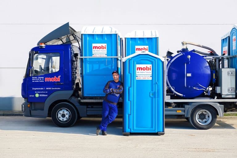 Ein Mann lehnt sich an eine mobile mobi Toilette vor einem Fahrzeug.