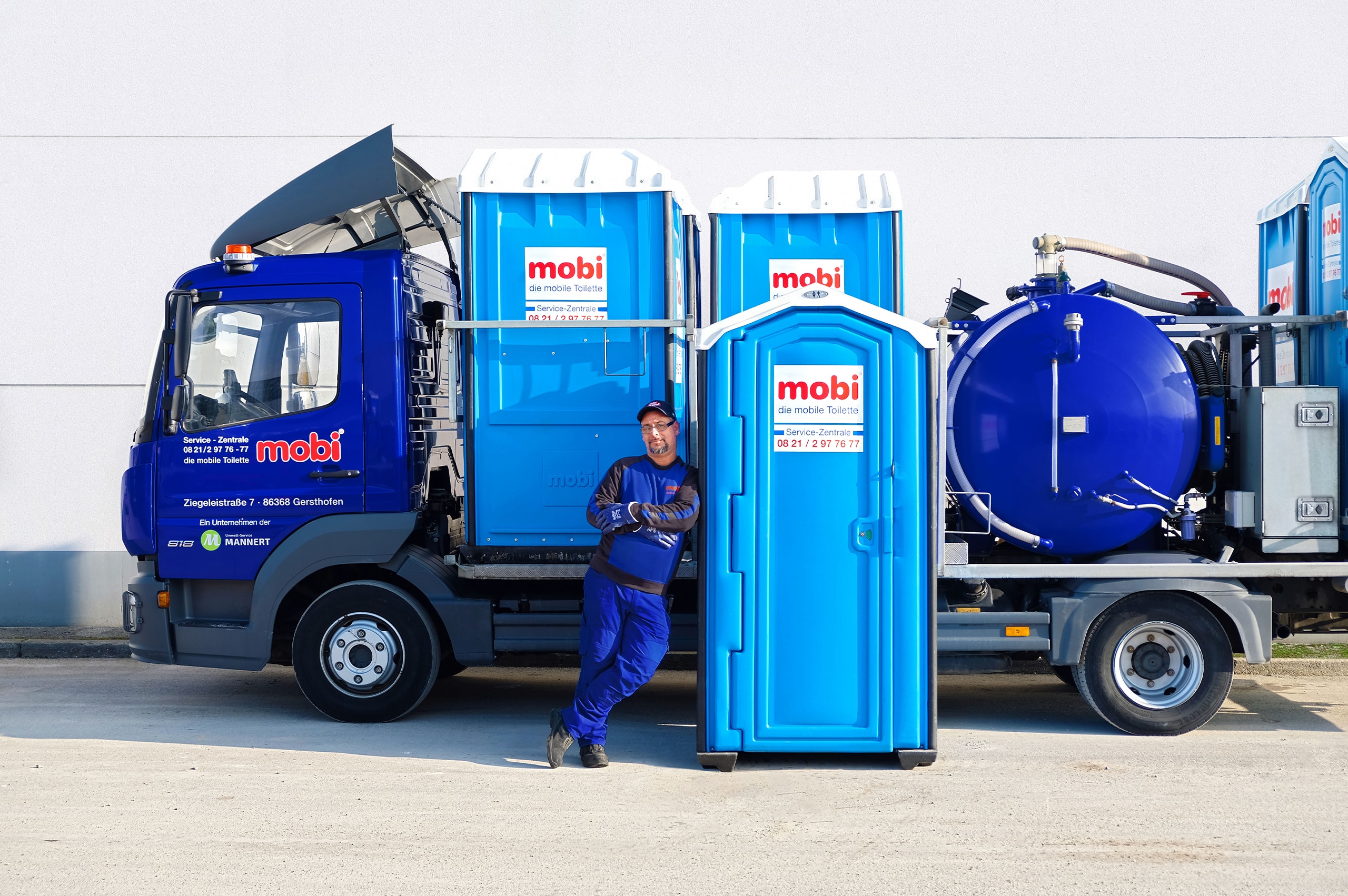 Ein Mann lehnt sich an eine mobile mobi Toilette vor einem Fahrzeug.