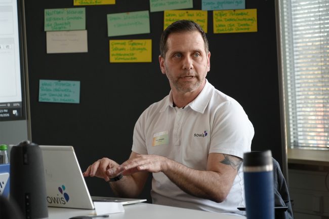 tegos-sowis-gmbh-als-transformationspartner-beim-vediso-netzwerkevent-2026-ki-strategisch-denken-und-praktisch-einsetzen Ein Mann tipp auf seinem Laptop vor grauer Wand mit Notizen.